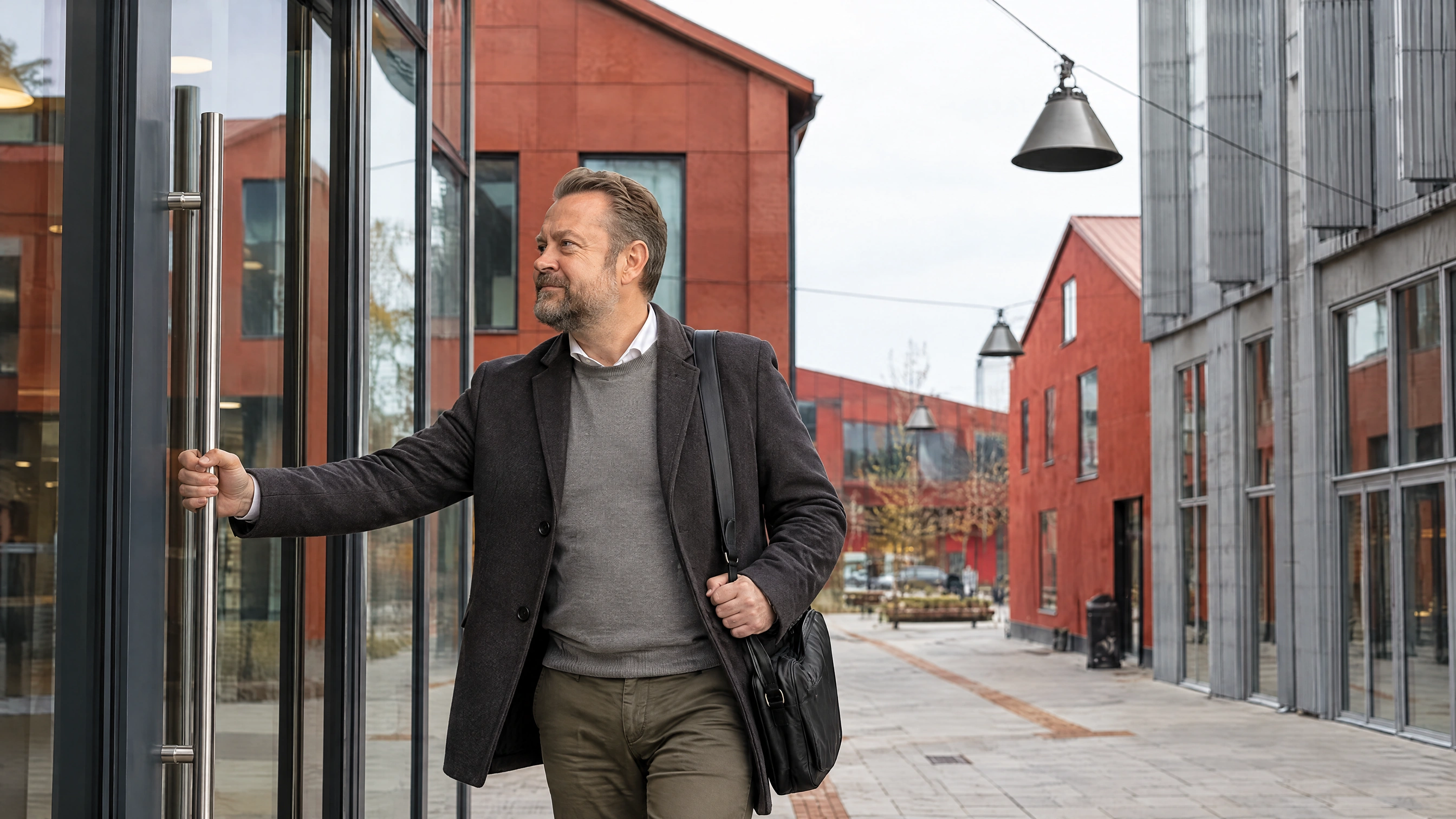 En mand i frakke og med skuldertaske åbner glasdøren ind til arbejdet